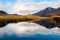 Удивительный шотландский пейзаж спокойного озера с зеркальной поверхностью, отражающей гору с заснеженной вершиной и голубым облачным небом в районе Глен-Коу — стоковое фото