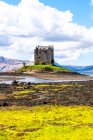 Paisaje primaveral brillante con castillo de piedra medieval situado en la colina cerca del río en el valle verde en las tierras altas escocesas en el día soleado con cielo nublado - foto de stock
