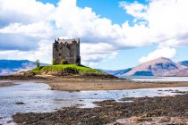 Paisaje primaveral brillante con castillo de piedra medieval situado en la colina cerca del río en el valle verde en las tierras altas escocesas en el día soleado con cielo nublado - foto de stock