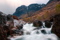 Жорсткий природний ландшафт з гірською річкою, що протікає між скелястими височинами в похмурий день у Шотландії. — стокове фото