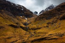 Malerischer Blick auf Berghang mit Schnee bedeckt zwischen grünen Hügeln mit Wald gegen bewölkten Himmel im Frühling Tag in den schottischen Highlands — Stockfoto
