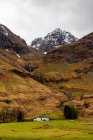 Malerischer Blick auf Berghang mit Schnee bedeckt zwischen grünen Hügeln mit Wald gegen bewölkten Himmel im Frühling Tag in den schottischen Highlands — Stockfoto