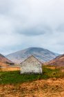 Casa de pedra envelhecida localizada na colina verde contra a majestosa montanha rochosa nas Terras Altas da Escócia — Fotografia de Stock