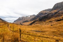 Estrada curvilínea estreita que atravessa terreno montanhoso com grama seca entre montanhas rochosas no dia nublado da primavera nas Terras Altas da Escócia — Fotografia de Stock