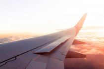 Vista da janela de asa de aeronaves modernas voando sobre nuvens densas durante o pôr do sol — Fotografia de Stock