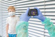 Medico irriconoscibile in guanti protettivi e uniforme con termocamera per il controllo della temperatura del bambino in strada durante l'epidemia di coronavirus — Foto stock