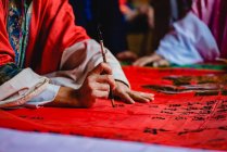 Erntemeister im Kimono bemalt schwarze Hieroglyphen mit Tinte auf rotem Textil im Tempel von Hongkong — Stockfoto