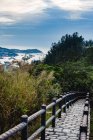 Picturesque view of green shore with bay and small path with fence and misty mountains under blue sky with clouds — Stock Photo
