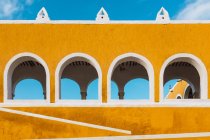 Exterior of vivid yellow walls with arches in ancient city of Izamal against blue sky — Stock Photo