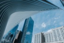 Знизу сучасних хмарочосів зі скляними дзеркальними стінами та футуристичною конструкцією на тлі блакитного неба — стокове фото
