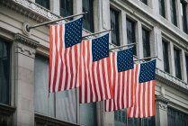 From below of vibrant national flags of USA hanging in row from stone building over street — Stock Photo