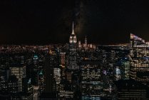 Veduta aerea di megalopoli con pareti di vetro illuminate e facciate futuristiche di alti skyline sullo sfondo la sera — Foto stock