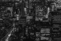 Vue aérienne de la mégalopole avec des murs de verre éclairés et des façades futuristes de grandes lignes de crête en arrière-plan le soir — Photo de stock