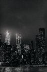 Schwarz-weißer Komplex moderner beleuchteter Skylines in Manhattan, der sich nachts vor dem ruhigen Fluss befindet — Stockfoto
