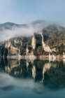 Magnificent landscape of calm lake with mirrored water surface surrounded by rough rocky mountains of Montsec Range covered with dense fog in cold day in Spain — Stock Photo
