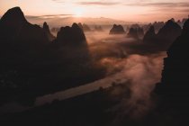 Le sagome di montagne alte grandi contro cielo nuvoloso lucente su mattina nebbiosa in Guilim — Foto stock