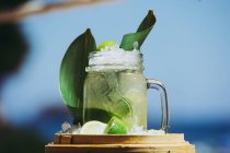 Glass mug with refreshing cold cocktail with fresh lime and green leaves — Stock Photo