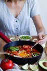 Unrecognizable female in dress sitting at table with various ingredients and enjoying fresh shakshuka with eggs and vegetables — Stock Photo
