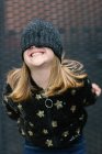 Enfant anonyme drôle en veste chaude et bonnet tricoté couvrant la moitié du visage debout à l'extérieur et souriant — Photo de stock