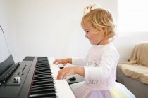 Side view of schoolgirl in fluffy skirt sitting at synthesizer and preparing for music class looking at camera — Stock Photo