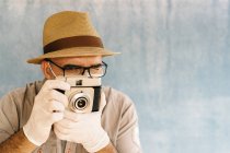 Homem de meia idade em luvas de látex e máscara médica tirar foto com câmera retro em estúdio de luz — Fotografia de Stock