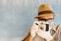 Homem de meia idade em luvas de látex e máscara médica tirar foto com câmera retro em estúdio de luz — Fotografia de Stock