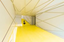 Жінка в повсякденному одязі сидить у футуристично-жовтому коридорі сходів з геометричними стінами та стелею — стокове фото