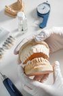 Сверху анонимный стоматолог в медицинских перчатках, работающий с зубным протезом в современной лаборатории — стоковое фото