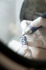 Зверху врожаю анонімний стоматолог в медичних рукавичках шліфує зубний протез професійним інструментом під час роботи в сучасній лабораторії — стокове фото