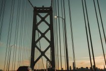 Famoso puente colgante de la bahía en San Francisco con coches en movimiento contra el cielo nublado durante la salida del sol - foto de stock