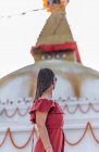 Vista laterale della donna in piedi vicino al tempio buddista con ghirlande decorative e torre sotto il cielo nuvoloso alla luce del giorno — Foto stock