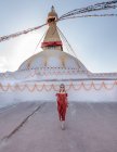 Mulher feliz olhando para a câmera de pé perto do templo budista com guirlandas decorativas e torre sob céu nublado à luz do dia — Fotografia de Stock
