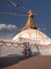 Coppia che si tiene per mano e si guarda in piedi vicino al tempio buddista con ghirlande decorative e torre sotto il cielo nuvoloso alla luce del giorno — Foto stock