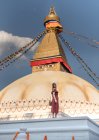 Щаслива жінка дивиться на камеру біля буддійського храму з декоративними садами і вежею під хмарним небом вдень. — стокове фото