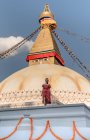 Mulher feliz olhando para a câmera de pé perto do templo budista com guirlandas decorativas e torre sob céu nublado à luz do dia — Fotografia de Stock