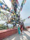 Vue latérale du couple en tenue décontractée marchant sur un remblai près d'anciens bâtiments bouddhistes sous une guirlande colorée avec des drapeaux le jour ensoleillé — Photo de stock