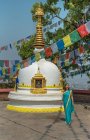 Touriste féminine en robe regardant loin tout en se tenant sur le trottoir près de vieux stupa hémisphérique en pierre avec coupole sur le dessus sous guirlande avec des drapeaux en été — Photo de stock
