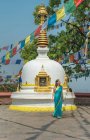 Touriste féminine en robe regardant loin tout en se tenant sur le trottoir près de vieux stupa hémisphérique en pierre avec coupole sur le dessus sous guirlande avec des drapeaux en été — Photo de stock
