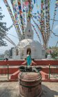 Touristinnen in Kleidern schauen weg, während sie auf dem Bürgersteig in der Nähe der alten halbkugelförmigen Stupa aus Stein mit Kuppel oben unter einer Girlande mit Fahnen im Sommer stehen — Stockfoto