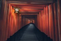 Fushimi Inari Taisha con camino de piedra rodeado de puertas rojas Torii e iluminado por linterna tradicional con persona distante irreconocible - foto de stock