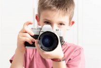 Criança bonito no desgaste casual tirar foto na câmera retro enquanto está em pé no apartamento moderno e divertido durante o fim de semana — Fotografia de Stock