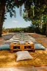 Terraço de verão com paletes de madeira em forma de mesas e almofadas aconchegantes preparadas para a celebração — Fotografia de Stock