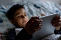 Niño encantado usando tableta en el dormitorio durante el fin de semana - foto de stock