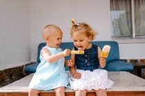 Симпатичні маленькі дівчата їдять смачні ескізи, насолоджуючись літом і сидячи разом на подвір'ї — стокове фото