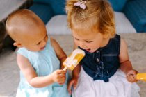 Nette kleine Mädchen essen leckere Eis am Stiel, während sie den Sommer genießen und zusammen im Hinterhof sitzen — Stockfoto