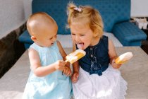 Симпатичні маленькі дівчата їдять смачні ескізи, насолоджуючись літом і сидячи разом на подвір'ї — стокове фото