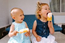 Petites filles mignonnes mangeant délicieux popsicles tout en profitant de l'été et assis ensemble dans la cour arrière — Photo de stock