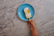 Top view of cropped unrecognizable kid hand grabbing a delicious fruit popsicle placed on table — Stock Photo