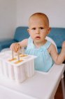 High angle of cute toddler sitting on high chair on terrace and eating delicious popsicles while looking at camera — Stock Photo