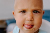 Милый маленький ребенок смотрит в камеру с грязным ртом наслаждаясь вкусным домашним фруктовым мороженым во время отдыха на террасе — стоковое фото
